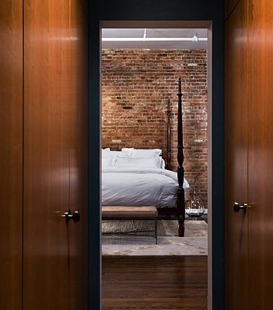 Brick-Wall-Studio-Apartment-by-Stephan-JAKLITSCH-GARDNER-narrow-hall-to-uncovered-four-poster-bed-on-area-rug-with-white-linen.jpeg