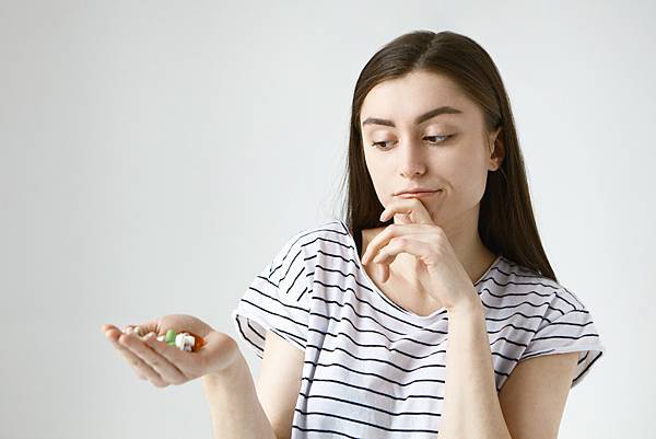 isolated-indecisive-doubtful-young-lady-with-loose-dark-hair-rubbing-chin-thoughtfully-looking-colorful-pills-her-palm-going-take-them.jpg