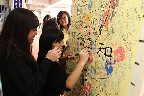 景女學生在手印牆上蓋滿學生比「五」的手印，並請同學踴躍簽名蓋印，象徵「手」護兒童健康。(台灣世界展望會提供)