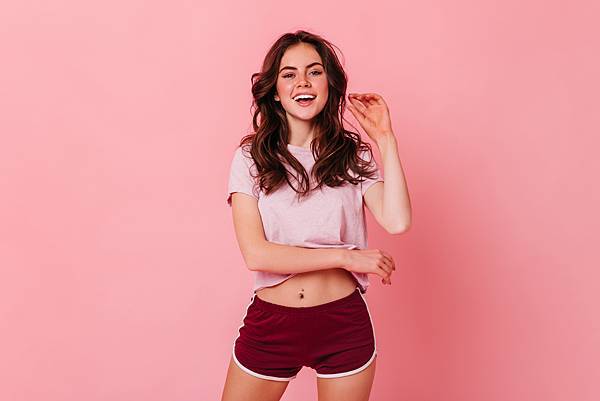 attractive-curly-dark-haired-woman-t-shirt-shorts-is-smiling-pink-wall