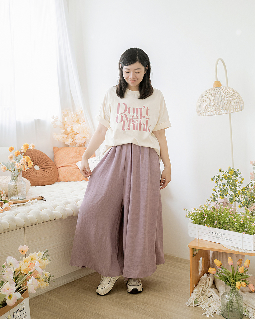 棉花糖女孩身穿白色字母T恤與薰衣草紫寬褲，搭配白色球鞋，站在自然光充足的房間中，展現大尺碼女裝的清新甜美風格，適合夏季穿搭與日系造型
