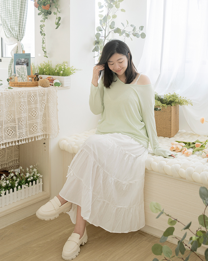 棉花糖女孩坐在花草環繞的室內空間，身穿薄荷綠針織上衣與白色層次裙，搭配白鞋，展現2025夏季穿搭的甜美風格與日系度假感