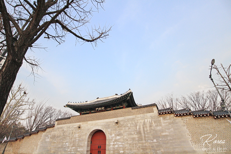 경복궁의 성벽과 나무의 이미지, 겨울철 한국 전통 건축물을 배경으로 평화로운 아침 하늘.